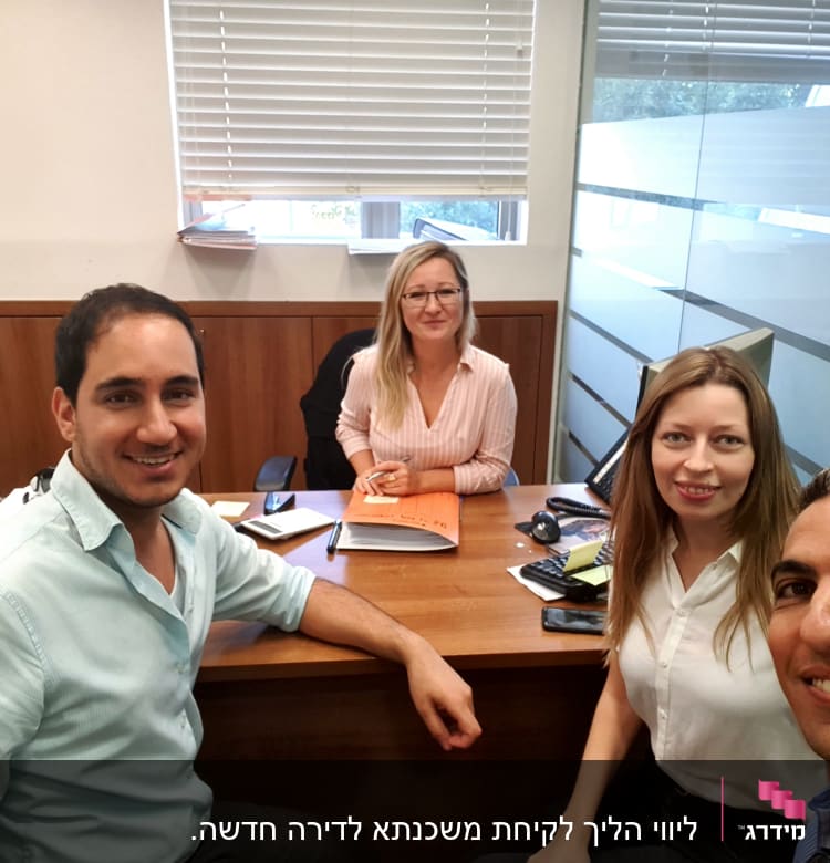 ארבעה אנשים יושבים סביב שולחן עם מחשב ומסמכים